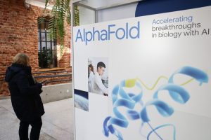 A person walks past the AlphaFold logo on a display board at a conference.
