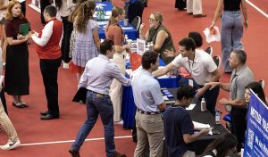 Students shaking hands and meeting with employers at tables at a large career fair; overhead shot.