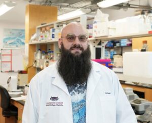 Portrait of Ian Gaudet wearing a lab coat in a laboratory.