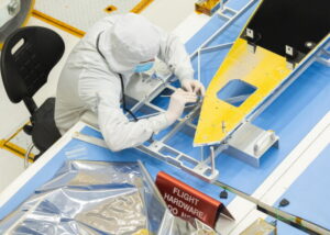 A person in a white lab outfit works on a metal piece.